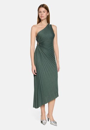 Grøn kjole med ét skulderstrop og plisseret tekstur samt et twist-detalje ved taljen. Midilængde med asymmetrisk kant. Sølvfarvede hæle.