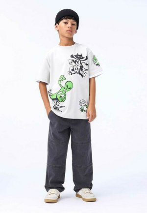 Hvid kortærmet t-shirt med grønne og sorte grafiske designs, parret med mørkegrå løstsiddende bukser og hvide sneakers.