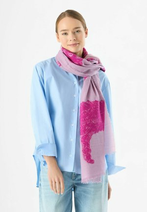 Écharpe rose clair avec un motif de chat rose vif, bordures frangées, portée sur une chemise bleue, mettant en valeur la texture textile fine et les superpositions.