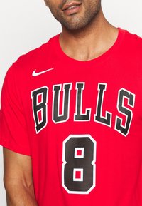 Camiseta de algodón roja con la palabra "BULLS" en letras negras en negrita y el número "8" debajo. Logotipo de Nike en blanco en el hombro izquierdo.