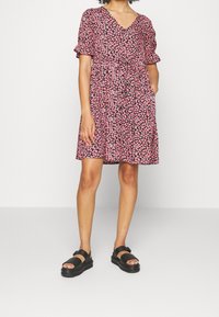 Krátký rukáv, šaty ke kolenům s hlubokým výstřihem, černý základ a růžový květinový vzor. Obsahuje stažený pas a boční kapsy.