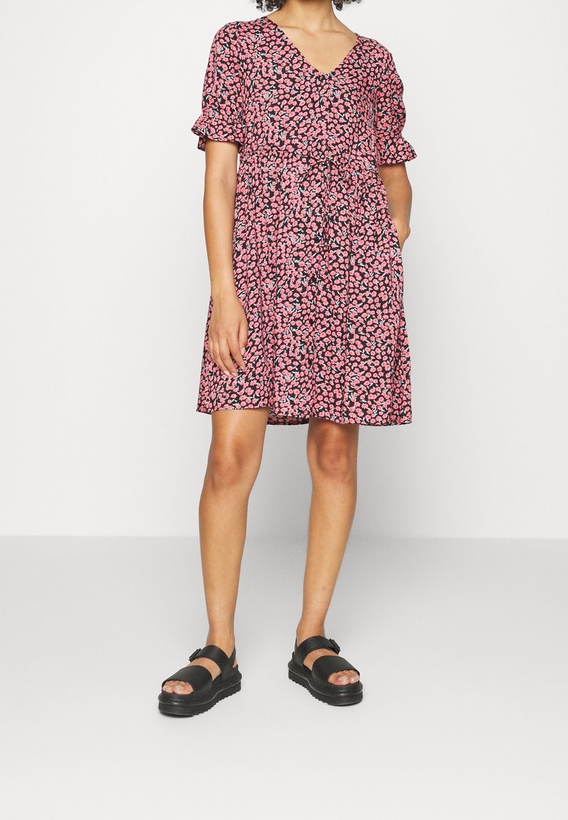 Krátký rukáv, šaty ke kolenům s hlubokým výstřihem, černý základ a růžový květinový vzor. Obsahuje stažený pas a boční kapsy.