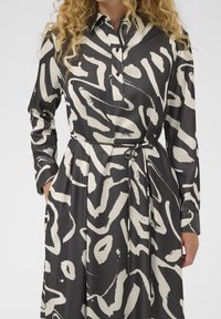 Schwarzes und weißes gemustertes Kleid mit langen Ärmeln, einem Kragen und einer taillierten Taille, aus einem glatten, leichten Stoff.