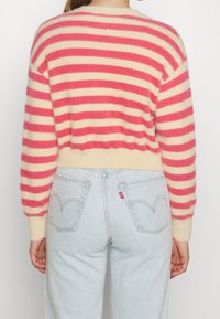 Růžový a krémový pruhovaný svetr s huňatou texturou, zkráceným střihem a žebrovaným lemem, kombinovaný s světle modrými džínami s vysokým pasem.