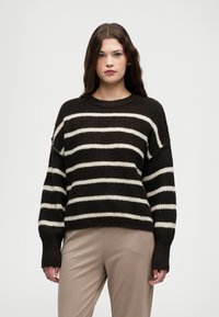 Χοντρή πλεκτή μπλούζα σε σκούρο καφέ χρώμα με φαρδιές λευκές ρίγες. Διαθέτει στρογγυλή λαιμόκοψη και κρεμαστούς ώμους. Μαλακή υφή και χαλαρή εφαρμογή.