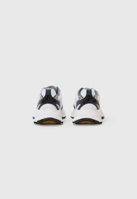 White athletic shoes with black and gray accents, featuring a mesh upper, padded collar, and textured rubber sole with yellow detail.