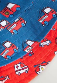Sombrero tipo cubo de algodón, con una sección azul que presenta camiones de bomberos rojos y una sección roja con vehículos de emergencia y helicópteros, textura acolchada.