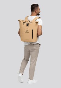 Mochila roll-top de color marrón hecha de material impermeable, con correas ajustables, un logo y un bolsillo con cremallera lateral para un acceso fácil.