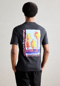 Sort bomulds T-shirt med et farverigt, abstrakt træ grafik på ryggen, med "Scotch & Soda Amsterdam" tekst i pink og hvid.