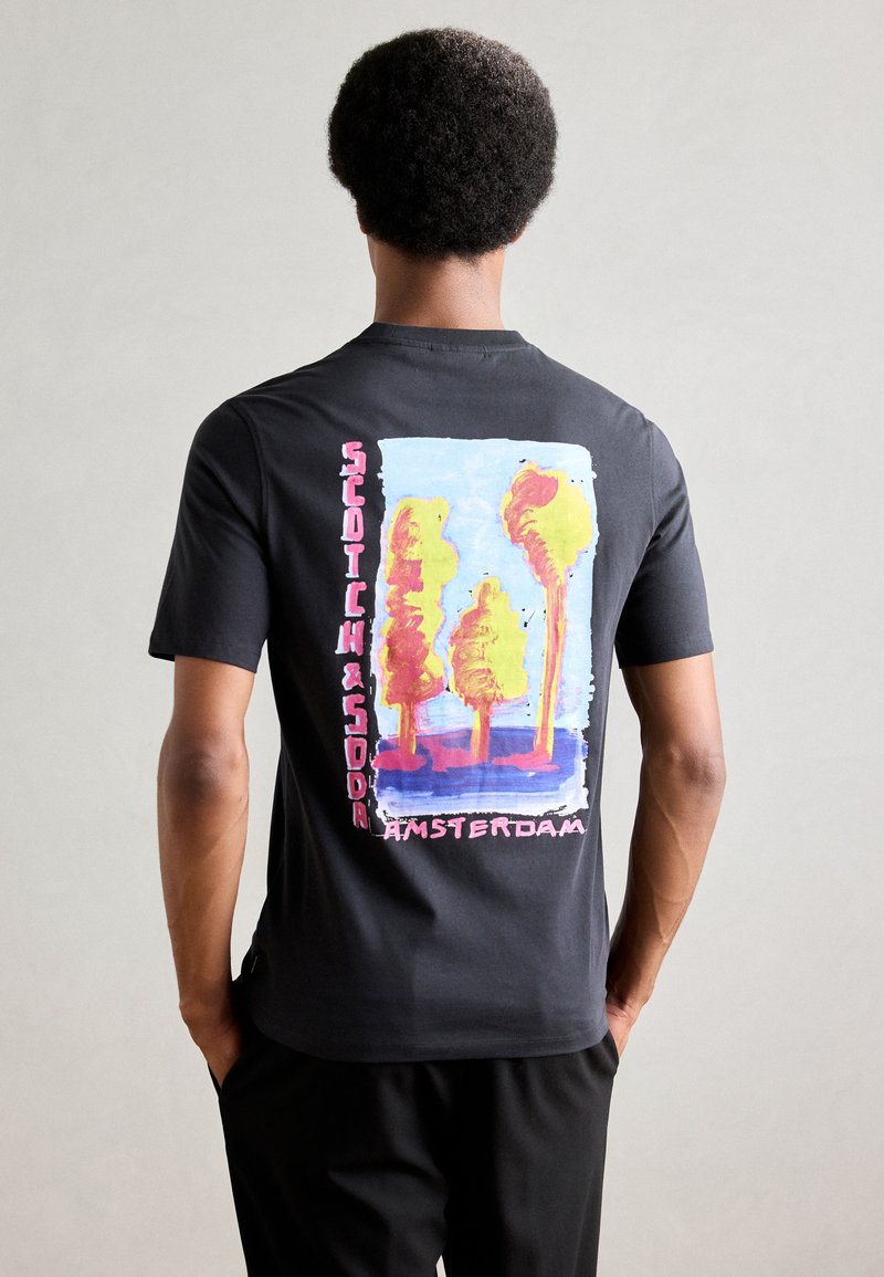 Sort bomulds T-shirt med et farverigt, abstrakt træ grafik på ryggen, med "Scotch & Soda Amsterdam" tekst i pink og hvid.