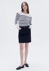 Camiseta de manga larga a rayas en blanco y azul marino, combinada con una falda de mezclilla oscura con bolsillos frontales y costuras doradas. Mocasines negros completan el conjunto.