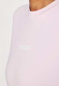 Camiseta de algodón de color rosa claro con cuello redondo y mangas cortas, que presenta el logo en blanco de "adidas" en la parte frontal con una textura suave.