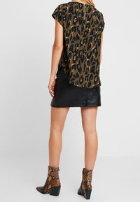Tierdruckbluse in Grün, Schwarz und Gold mit kurzen Ärmeln, kombiniert mit einem schwarzen Leder-Minirock und braunen Schlangenleder-Stiefeletten.