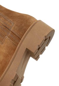 Botín de ante marrón con suela de goma gruesa, patrón de tracción texturizado y detalles de costura lateral.