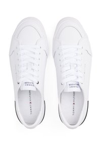 Bílé tenisky s hladkým syntetickým svrškem, kulatou špičkou, plochými tkaničkami a značkovou stélkou. Obsahují jemné černé akcenty na podrážce.