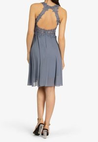 Sukienka na okrągłym dekolcie, bez rękawów, uszyta z miękkiego szarego szyfonu z misternym koronkowym wykończeniem z tyłu. Posiada zwiewny dół oraz sandały na cienkich obcasach.