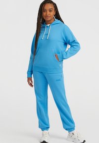 Set di felpa e pantaloni della tuta blu chiaro in morbido tessuto con vestibilità comoda. La felpa presenta una tasca anteriore e lacci a contrasto; i pantaloni hanno polsini elasticizzati.