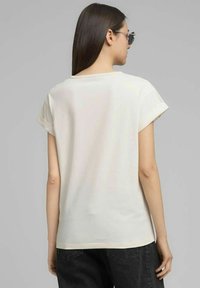 Maglietta a maniche corte color crema con vestibilità rilassata e risvolti arrotolati, realizzata in tessuto morbido, caratterizzata da una scollatura arrotondata e una trama liscia.