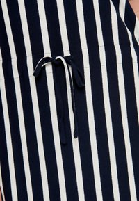 Tecido listrado em azul-marinho e branco com detalhe de cordão regulável. Apresenta listras verticais e uma textura suave, adequada para uso casual.