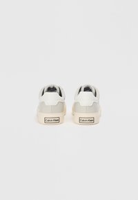 White and light grey sneakers with smooth leather, rounded design, thick off-white sole, and a black "Calvin Klein" logo on the heel.