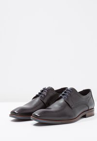 Black leather dress shoes with a smooth texture, pointed toe, and blue lace accents. Features subtle stitching and a brown sole.