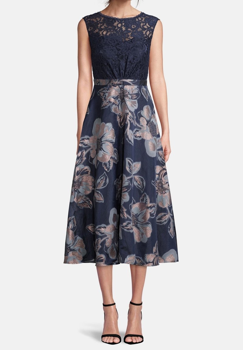 Robe florale bleu marine avec un corsage en dentelle, une taille ajustée et une jupe évasée, présentant de grands motifs floraux en tons bronze et bleu doux.