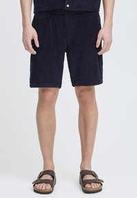 Marineblå cordcordshorts med teksturert overflate, kne-lange, har en snøring i livet og er kombinert med brune sandaler.