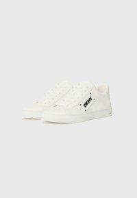 Hvite sneakers laget av glatt materiale, med et lavt design, snøring og en svart logoakcent på siden.