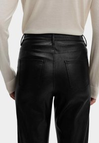 Černé kalhoty z umělé kůže s hladkým povrchem, vybavené dvěma zadními kapsami, poutečky na opasek a vysokým pasem.