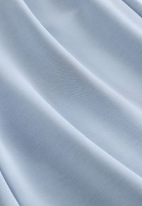 Tissu bleu clair avec une texture lisse légèrement plissée, montrant de fines fibres tissées et des ombres douces.