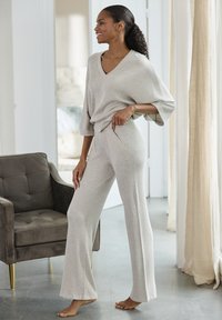 Lichtgrijze, geribbelde loungewear set met een oversized V-hals top en wijde broek met zijzakken, gedragen tegen een neutrale achtergrond.