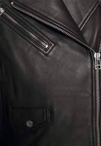 Černá kožená motocyklová bunda s diagonálními zipy, kapsou na prsou se zapínáním na patentku a texturovanou hladkou látkou.