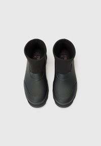 Une paire de bottes noir en caoutchouc imperméables avec des manches en néoprène au niveau des chevilles, vues de dessus sur un fond blanc.