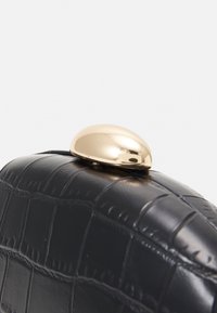 Bolso de mano de cuero negro efecto cocodrilo con un cierre redondeado dorado en la parte superior, superficie texturizada y bordes definidos.