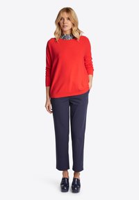 Roter Pullover, marinefarbene Hose und blaue Schuhe. Der Pullover hat einen runden Ausschnitt und lange Ärmel; die Hose hat einen geraden Schnitt und eine glatte Textur.