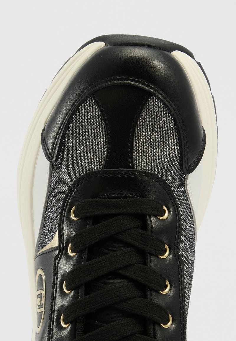 Schwarzer und grauer Sneaker mit Obermaterial aus Leder und strukturiertem Stoff, goldenen Ösen, schwarzen Schnürsenkeln und einer cremefarbenen Gummisohle.