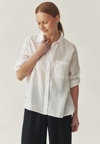White linen shirt with a button-down front, single chest pocket, and rolled-up sleeves; relaxed fit and lightweight texture.