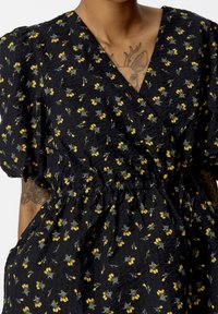 Top avvolgente nero a fiori con motivi gialli e grigi, maniche a sbuffo, tessuto testurizzato e vita elastica per una vestibilità arricciata.