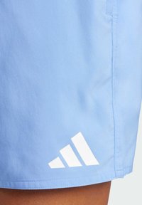 Svetlomodré športové šortky s hladkou textúrou, s bielym logom Adidas v trojuholníkovom dizajne na leme.