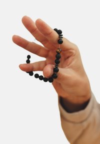 Juodas karoliukų apyrankė su įvairiais tekstūriniais paviršiais, įskaitant matinį ir blizgantį apdailą, sudaryta iš apvalių ir cilindrinių karoliukų.