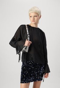 Svart gjennomsiktig bluse med lange ermer, kombinert med et miniskjørt med paljetter i blått og svart. Tilbehør med en liten sølvveske.
