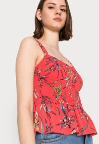 Top peplum com estampado floral vermelho, com corpete franzido e alças finas. Apresenta padrões de flores vibrantes e multicoloridas, e uma textura de tecido leve.