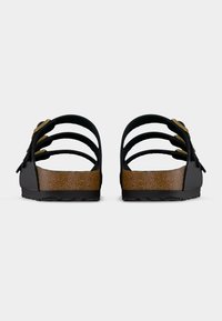Paire de sandales noires à trois brides avec semelles en liège marron et boucles dorées, vues de dos sur fond blanc uni.