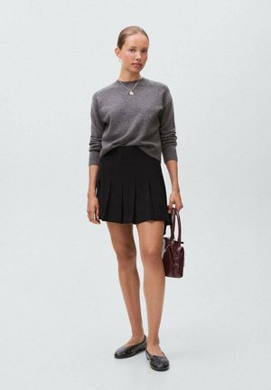 Pull gris, jupe plissée noire, ballerines noires avec des clous, et un petit sac à main bordeaux. Design simple axé sur des couleurs neutres.
