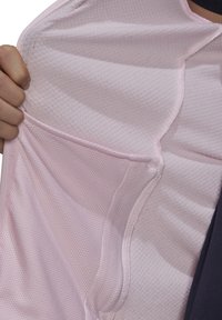 Main tenant ouvert un vêtement en tissu texturé rose clair montrant sa doublure en mesh respirant à l'intérieur.