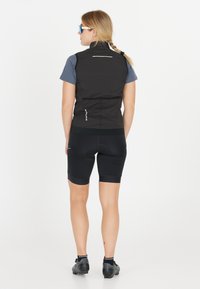 Sort ærmeløs vest med en glat tekstur, refleksaccent på ryggen, parret med sorte cykelsHORTS. Blå sports solbriller.