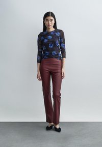 Top nero a maniche lunghe con motivo floreale blu, abbinato a pantaloni aderenti in pelle bordeaux. Scarpe nere completano il look. Texture liscia.