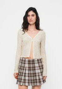 Ανοιχτό μπεζ μακρυμάνικη κορυφή με ριμπ υφή και V-λαιμόκοψη, με κοντό μήκος και σκάλωτες άκρες, συνδυασμένη με καρώ μίνι φούστα σε καφέ αποχρώσεις.