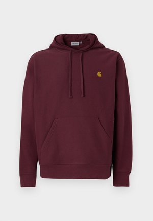 Burgundijas krāsas hoodie no mīkstas auduma ar kangoru kabatu, kapuci ar auklu un izšūtu zelta logotipu. Iezīmē ribotās piedurknes un apakšmali.