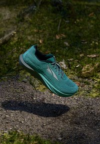 Scarpa da corsa turchese con tomaia in rete, lacci piatti e suola verde chiaro. Presenta un logo sul lato e una superficie texturizzata.